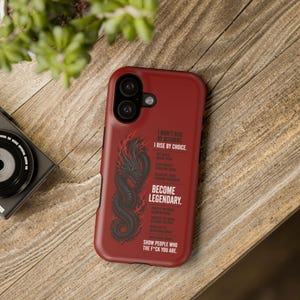 May include: A red phone case featuring a black dragon design with the text "I DIDN'T RISE BY ACCIDENT, I RISE BY CHOICE. BECOME LEGENDARY. SHOW PEOPLE WHO THE F*CK YOU ARE." The case is on a wooden surface.