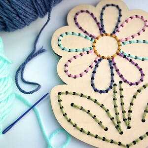 K&ouml;nnte beinhalten: Ein Holz-Blumen-Stickset mit vorgebohrten L&ouml;chern zum Sticken. Das Set enth&auml;lt gr&uuml;nes, blaues, rosa und gelbes Garn und eine Nadel.