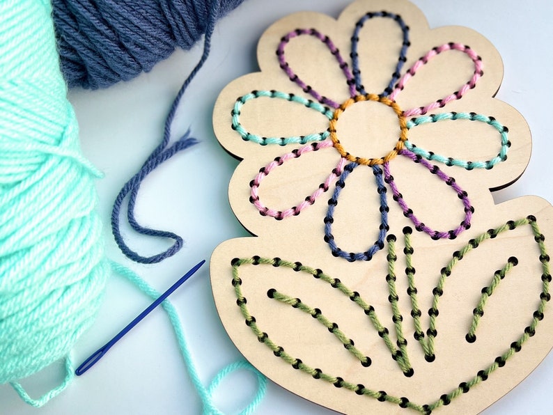 K&ouml;nnte beinhalten: Ein Holz-Blumen-Stickset mit vorgebohrten L&ouml;chern zum Sticken. Das Set enth&auml;lt gr&uuml;nes, blaues, rosa und gelbes Garn und eine Nadel.
