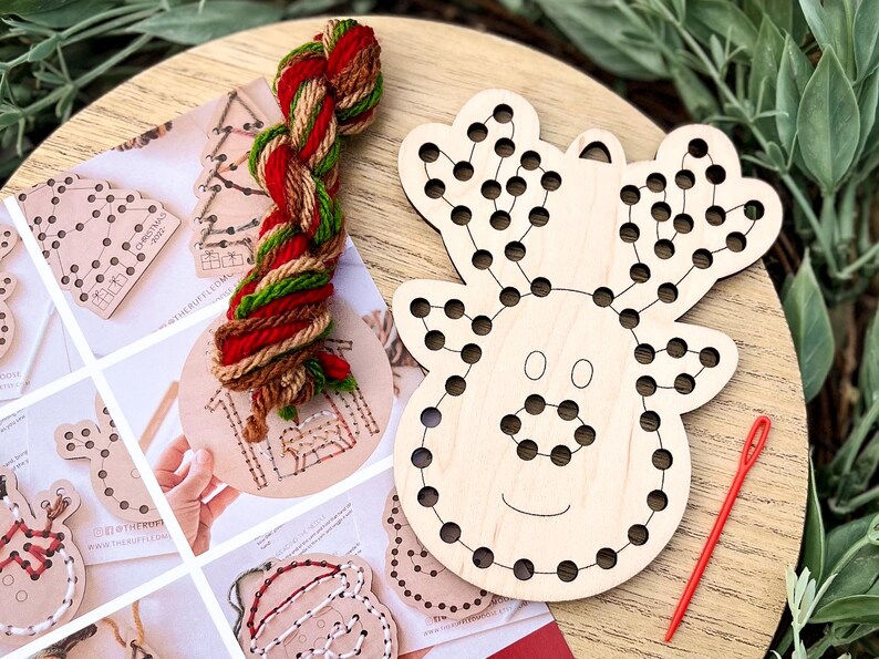 May include: A wooden reindeer-shaped craft with pre-drilled holes for string art, accompanied by a red needle and a skein of red, green, and brown yarn. Additional wooden ornaments and instructions are visible.