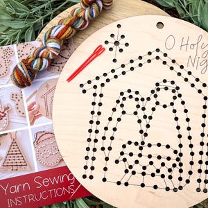 May include: A wooden Christmas craft kit featuring a circular wooden board with a nativity scene design, the words "O Holy Night", and a star. Includes yarn, needles, and instructions for a yarn sewing project.
