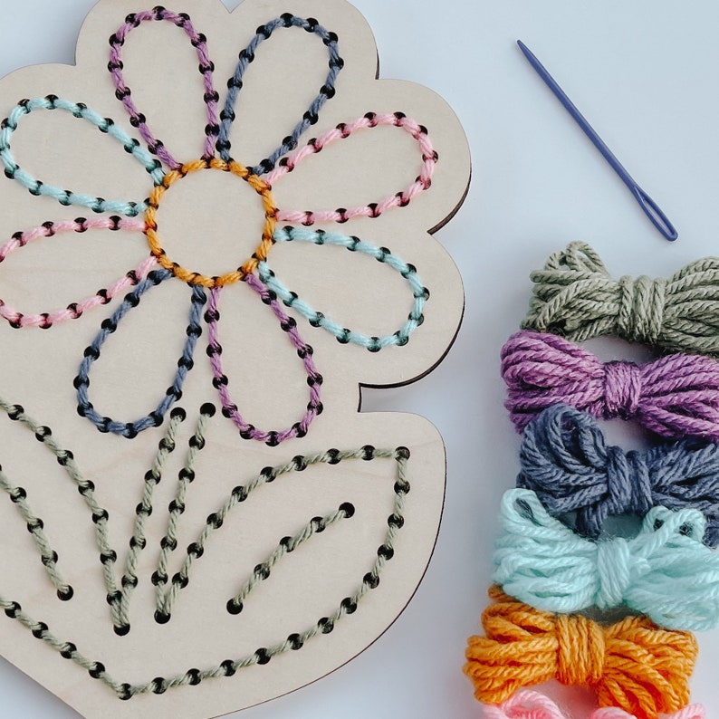 K&ouml;nnte beinhalten: Holz-Bastelset in Form einer Blume mit buntem Stickgarn zum Sticken. Das Set enth&auml;lt eine Holzblume mit vorgebohrten L&ouml;chern und einer Nadel.