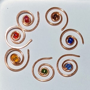 May include: Seven copper wire spirals with colourful glass beads in the centre. The beads are red, orange, yellow, green, blue, and purple.