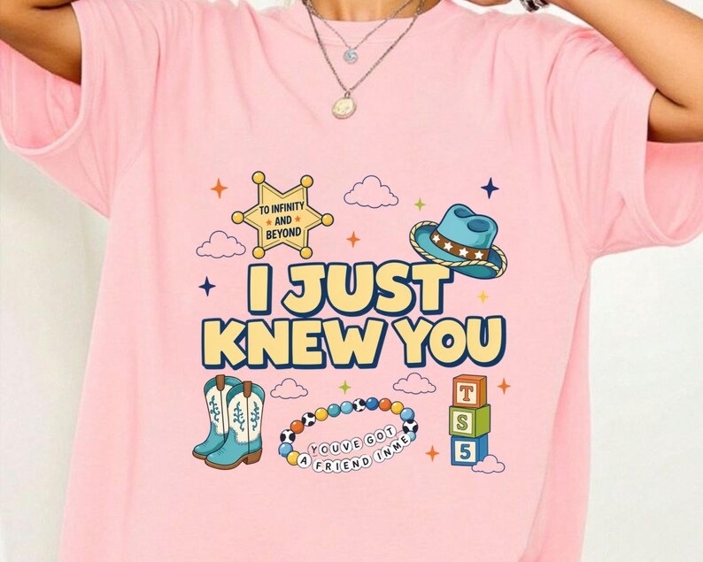 May include: A light pink t-shirt featuring a graphic print with the text I JUST KNEW YOU, a sheriff badge with TO INFINITY AND BEYOND, a blue cowboy hat, cowboy boots, a colorful beaded bracelet with YOU'VE GOT A FRIEND IN ME, and toy blocks.