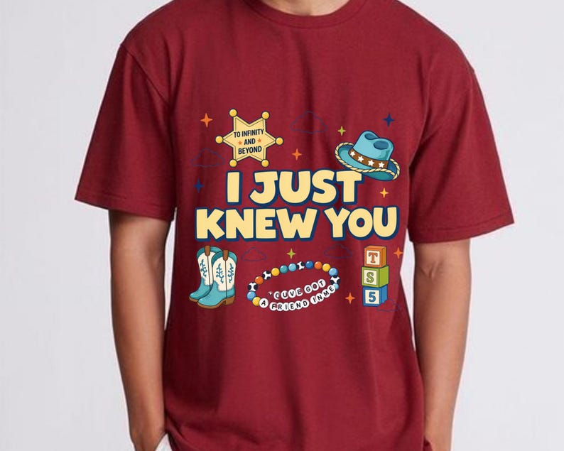 May include: A maroon short-sleeved t-shirt featuring the yellow text I JUST KNEW YOU. Graphics include a yellow sheriff badge with TO INFINITY AND BEYOND, a blue cowboy hat, light blue boots, a colorful beaded bracelet, and three stacked alphabet blocks.
