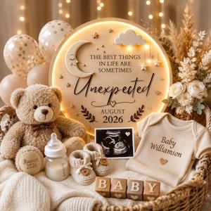 May include: A round wooden sign with warm LED lighting, featuring a crescent moon, cloud, and the text "THE BEST THINGS IN LIFE ARE SOMETIMES Unexpected AUGUST 2026". Includes a teddy bear, baby onesie, booties, baby bottle, and ultrasound photo.