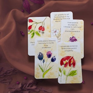 May include: A set of five rectangular affirmation cards featuring watercolor illustrations of flowers and berries. Each card displays printed text including phrases like I invite peace, harmony in my life now and forever and I always see evidence of abundance and prosperity.