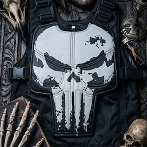 Könnte beinhalten: Schwarze taktische Weste mit weißem Totenkopf-Motiv, umgeben von Totenköpfen, Masken und einer Skeletthand. Die Weste hat verstellbare Riemen und Schnallen. Das Thema ist gothisch und kantig.