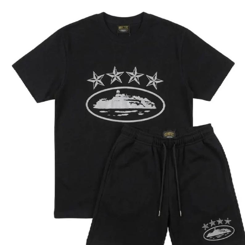 May include: Black t-shirt and shorts set. The shirt features a white graphic of stars and a landscape within an oval. The shorts have a matching design on the leg. The set is made of a soft material.