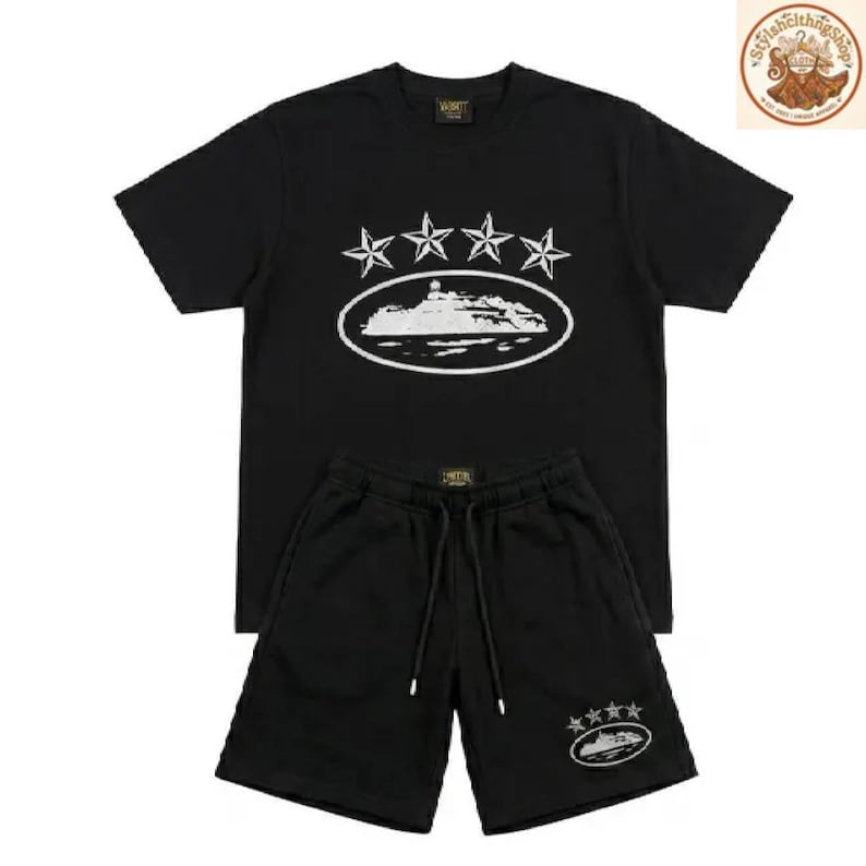 May include: Black t-shirt and shorts set. The t-shirt features a white graphic of stars and an oval design. The shorts have a drawstring and a matching oval graphic. The set is made of a soft material.