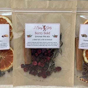 May include: Three simmer pot kits in clear bags. The kits contain dried orange slices, cinnamon sticks, and spices. Each kit has a label with the text "2 Spicy Girls" and a flavour name: Citrus Kick, Berry Bold, and Sweet Heat.