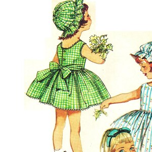 May include: Two girls wearing green and white gingham dresses with matching bonnets. The girl on the left is holding a bouquet of green leaves. The girl on the right is wearing a blue and white striped dress.
