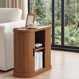 May include: A medium-brown wooden end table with a curved tambour sliding door, a flat top surface, and an open storage compartment featuring one shelf. The unit has a vertical slatted design on the front and side, with a black handle on the door.