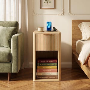 May include: A light wood nightstand featuring a single drawer with a vertical fluted front and a horizontal handle. The unit includes an open storage shelf at the bottom containing six stacked books with titles including Space and Design.