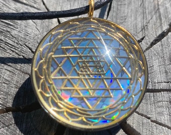 May include: A gold pendant necklace with a clear glass circle containing a gold Sri Yantra symbol. The pendant is on a black cord.