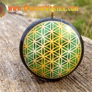 May include: A round, black pendant with a gold-colored loop at the top. The pendant features a green and gold flower of life design.