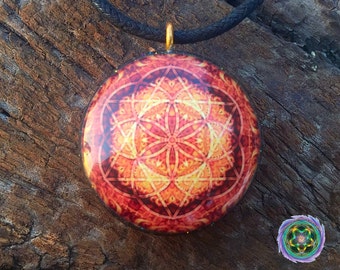 May include: A round, orange and yellow pendant with a geometric design, hanging from a black cord. The pendant is made of resin and features a flower of life pattern.