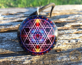 May include: A round pendant necklace with a black cord. The pendant features a colorful geometric design with a central blue eye.