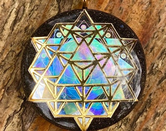 May include: A round pendant with a gold geometric design over a black base. The geometric design has iridescent colors of blue, green, and purple. The pendant hangs from a silver chain.