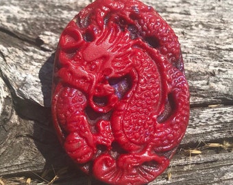 May include: A red carved dragon pendant with intricate details. The pendant is made of a smooth, polished stone and has a glossy finish.