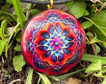 May include: A round pendant necklace with a colorful mandala design. The pendant is made of resin and features a geometric pattern with shades of red, blue, and pink.