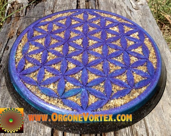 May include: A round, purple and gold resin coaster with a flower of life design. The coaster is on a wooden surface. www.orgonevortex.com