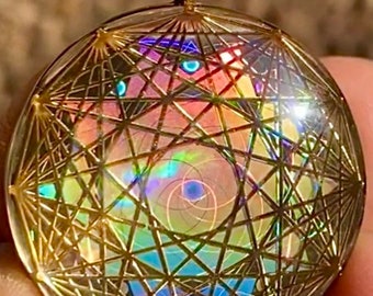 May include: A gold-toned pendant with a clear glass dome containing a geometric design with iridescent colors. The design features a spiral pattern and a variety of lines and shapes.