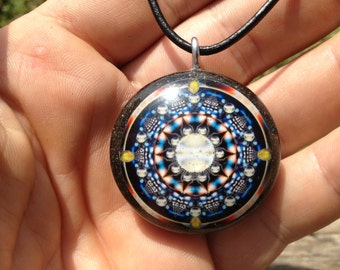 May include: A round pendant necklace with a black cord. The pendant features a colorful mandala design with a white center and a black background.