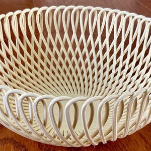 Peut inclure: Panier ovale de couleur crème avec un motif tissé. Le panier présente un motif répétitif de lignes courbes, créant un effet ajouré. Le panier est fait d'un matériau robuste et convient à divers usages.