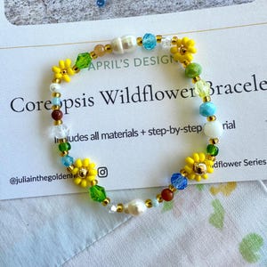 May include: A beaded bracelet with yellow daisy-shaped beads, pearls, and colorful glass beads. The bracelet is on a card that reads "Coreopsis Wildflower Bracelet" and "APRIL'S DESIGN".