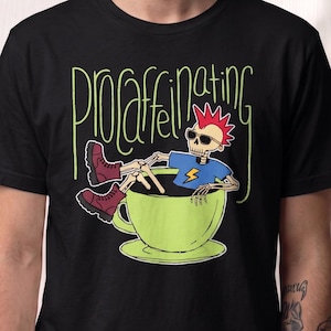 May include: Black t-shirt with the word "PROcaffeinating" in green script. The shirt features a cartoon skeleton with red hair and sunglasses, lounging in a green coffee cup. The skeleton is wearing a blue shirt with a yellow lightning bolt.