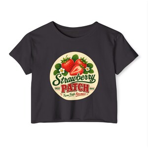 May include: A black crop top with a circular graphic featuring strawberries and the words "Strawberry Patch". The graphic includes the text "Sweet", "Smooth", and "Farm Fresh Feelings!"