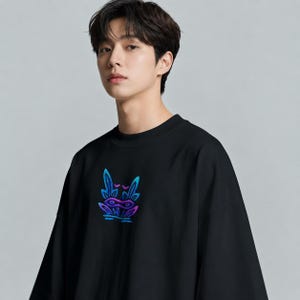 May include: A black crew neck t-shirt featuring a central graphic design of a stylized creature with pointed ears and a mask-like face. The graphic uses a vibrant gradient of blue, purple, and cyan colors, contrasting against the solid black fabric.