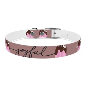 May include: A dog collar with a brown background and the word "joyful" in a cursive font. The collar features a repeating pattern of pink and brown ice cream cone illustrations. The collar has a silver buckle and hardware.