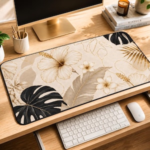 May include: A rectangular beige desk mat featuring a floral design with hibiscus flowers, leaves, and gold accents. The mat is placed on a wooden desk, with a keyboard and mouse visible.