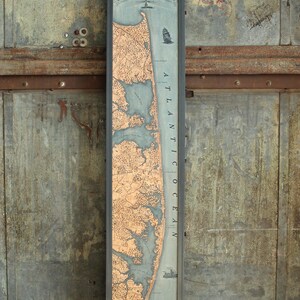 May include: A framed map of the Delaware and Maryland Atlantic Coast. The map features a detailed depiction of the coastline, with land areas in a tan hue and the ocean in blue. The frame is black, and the map includes nautical elements.