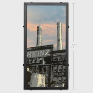 May include: A framed print featuring a black and white industrial scene with the word "HEINZ" visible. Two smokestacks are in the background, and the print measures 31 inches in height. The sky is a mix of blue and orange.