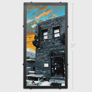 May include: A framed print of a brick building with the address 823 E. Fort Ave. The sky is blue and orange. The print is 31 inches tall.