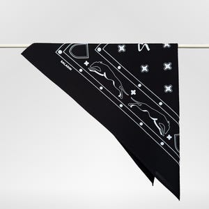 Könnte beinhalten: Schwarzes Bandana mit weißen geometrischen und tierischen Designs. Das Wort "SALADIN" ist weiß in der Ecke aufgedruckt. Das Bandana hängt an einer weißen Stange.