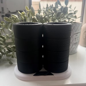 May include: Black miniature tires stacked on a white and black base. The tires are arranged in two stacks, one with smooth sides and the other with tread. The base is oval-shaped with a triangular cutout.