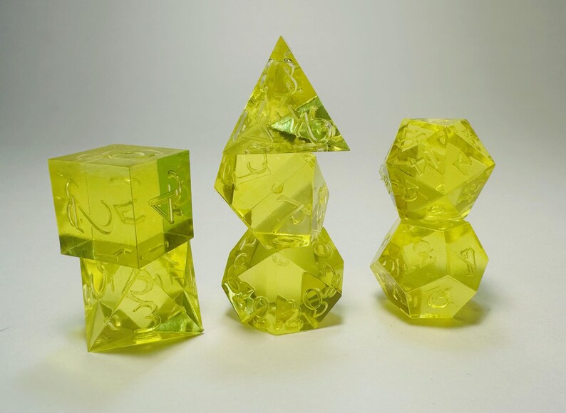 May include: A set of seven translucent neon yellow polyhedral dice arranged in three stacks. The dice feature engraved numbers and include a d4, d6, d8, two d10s, a d12, and a d20, all crafted from a clear, bright yellow resin material.