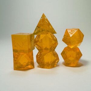 May include: A set of seven translucent orange polyhedral dice for tabletop gaming. The collection includes a d4, d6, d8, d10, d12, d20, and a percentile die, all featuring clear, etched numbers across their geometric surfaces.