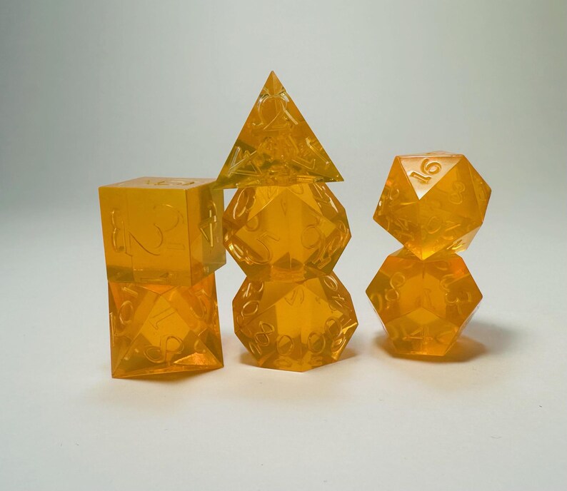 May include: A set of seven translucent orange polyhedral dice for tabletop gaming. The collection includes a d4, d6, d8, d10, d12, d20, and a percentile die, all featuring clear, etched numbers across their geometric surfaces.