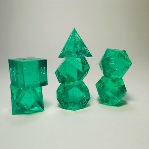 May include: A set of seven translucent emerald green polyhedral dice arranged in three stacks. The dice feature sharp edges and clear, recessed numbers. The collection includes a d4, d6, d8, d10, d12, and d20, all crafted from a smooth, see-through resin material.