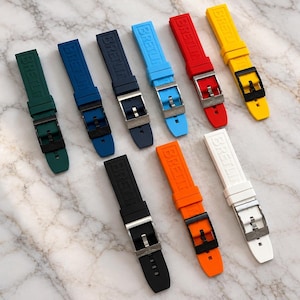 Puede incluir: Una colección de nueve correas de reloj de caucho en varios colores, incluyendo verde, azul, azul marino, azul claro, rojo, amarillo, negro, naranja y blanco. Cada correa presenta el texto en relieve BRETLIN y una hebilla de metal.