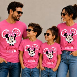 May include: Four people wearing matching pink t-shirts with a Minnie Mouse graphic and the text "Disney 2020". The shirts feature a large Minnie Mouse head design with a pink bow and stars. They are wearing blue jeans and sunglasses.
