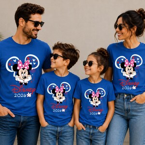 May include: A family of four wearing matching blue t-shirts featuring a Minnie Mouse graphic with a pink bow and the text "Disney 2026". The shirts are paired with blue jeans.