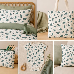 Puede incluir: Colección de artículos para el hogar y accesorios con temática de dinosaurios. Incluye un juego de cama, un bolso de mano, un body para bebé, un estuche y un cojín, todos con un patrón repetido de dinosaurios verde azulado sobre un fondo crema. También hay una figura de dinosaurio de madera.