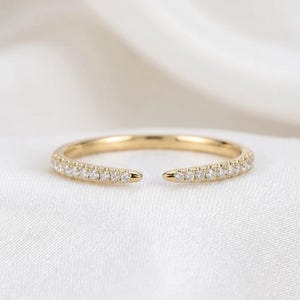 Peut inclure: Une bague ouverte en or dotée d'un anneau fin orné d'une rangée de petites pierres claires et scintillantes de chaque côté. La bague présente une finition métallique polie et une ouverture au centre, offrant un design délicat et raffiné.