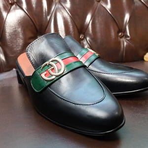 Front view of luxury black leather clogs featuring a gold-tone buckle.